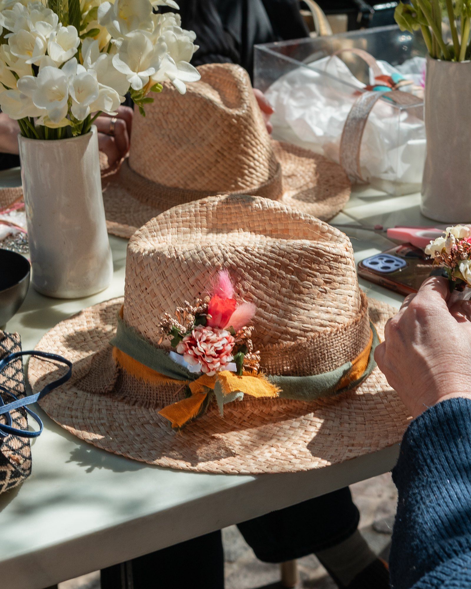 Sombrero de paja con cinta verde, moño amarillo y flores secas, sobre la mesa.